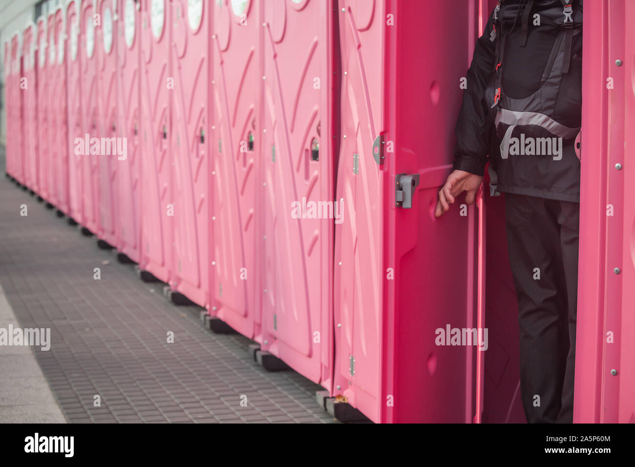 Ein Mann, der in einer sehr langen Reihe von Rosa mobile Toiletten. Stockfoto
