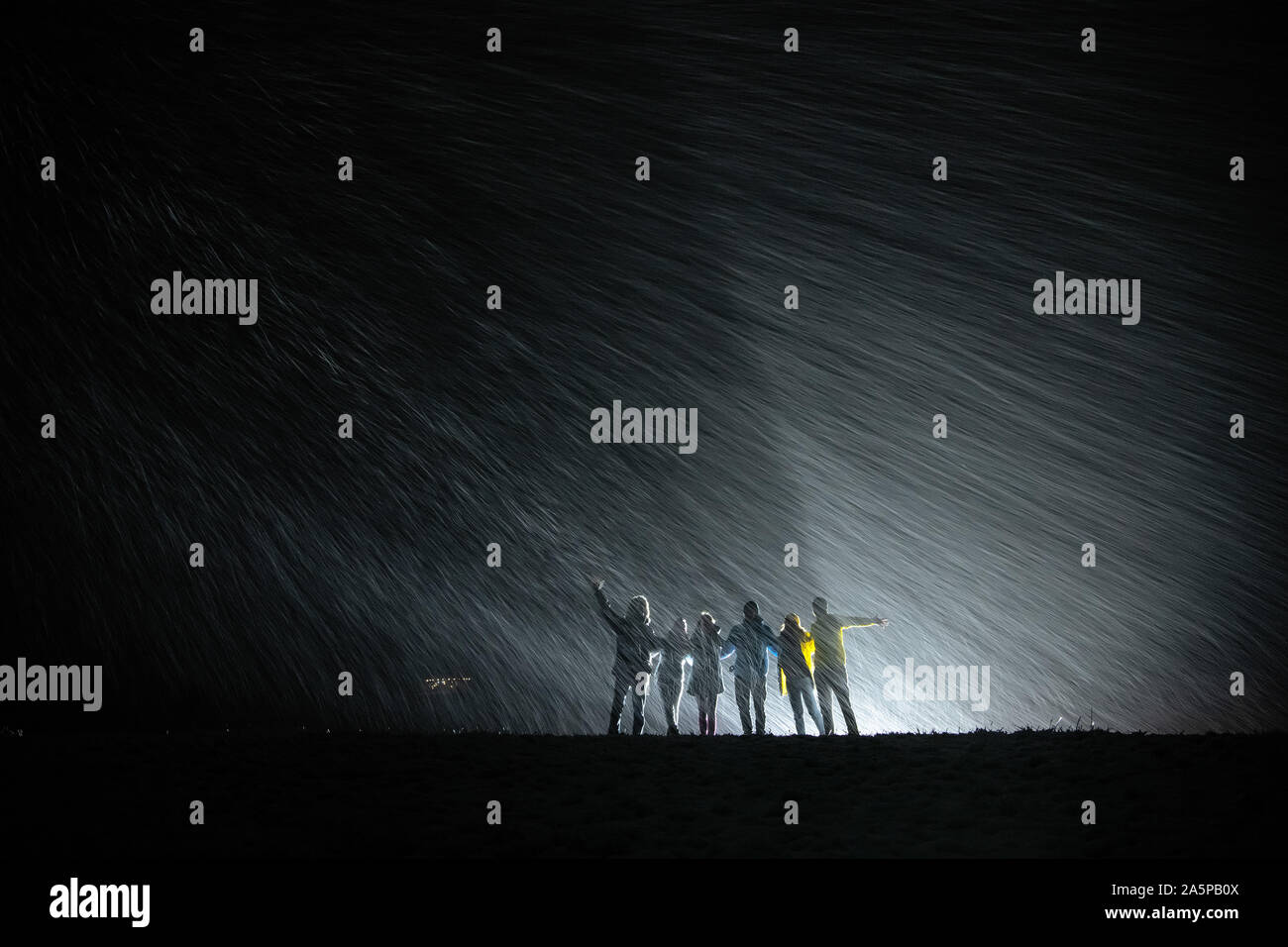 Gruppe von Silhouetten steht gemeinsam gegen Schneefall und wieder Licht und Spaß Stockfoto