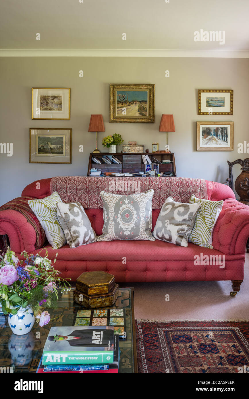Grau Kissen auf rosa Chesterfield mit gerahmten Kunstwerken. Stockfoto