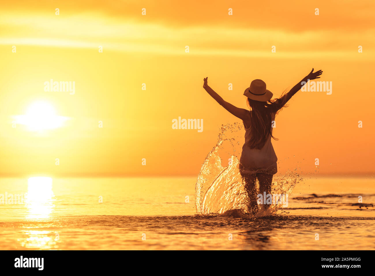 Slim's girl Silhouette mit erhobenen Armen gegen Sonnenuntergang am ruhigen Meer Strand Stockfoto