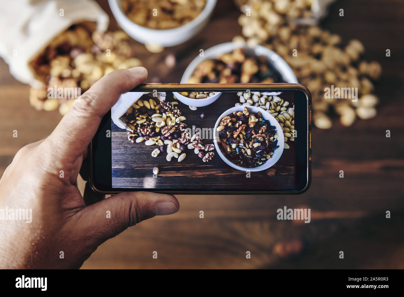 Essen blogger nimmt Foto für Blog, pic, Auswahl der vielfältigen Schalenfrüchte und getrocknete Früchte in weißen Schalen und sackleinen Säcke auf einem Holztisch, gesundes Essen con Stockfoto