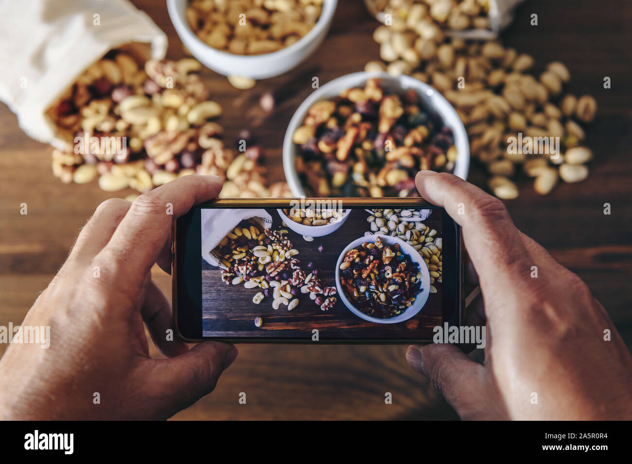 Essen blogger nimmt Foto für Blog, pic, Auswahl der vielfältigen Schalenfrüchte und getrocknete Früchte in Schalen und Tuch Säcke auf einem Holztisch, gesunde Ernährung Konzept ein Stockfoto