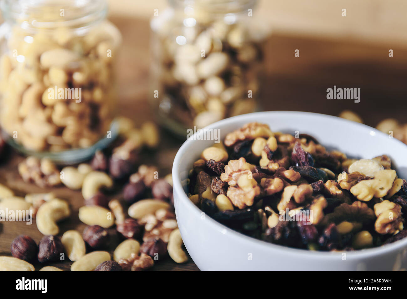 Weiße Schüssel mit abwechslungsreichen Bio Trockenfrüchte und Gläser mit gemischten Nüssen im Hintergrund auf rustikalen Holztisch, gesunde Speisen und Snacks - Konzept, c Stockfoto
