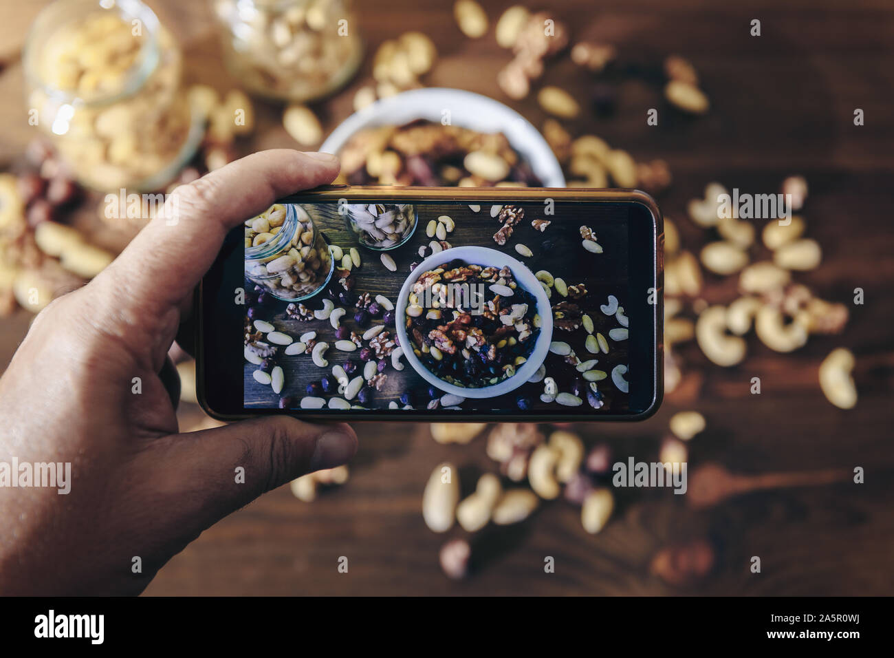 Essen blogger nimmt Foto für Blog, pic von einer weißen Schüssel mit abwechslungsreichen Bio Trockenfrüchte und Gläser mit gemischten Nüssen auf rustikalen Holztisch, gesunde f Stockfoto