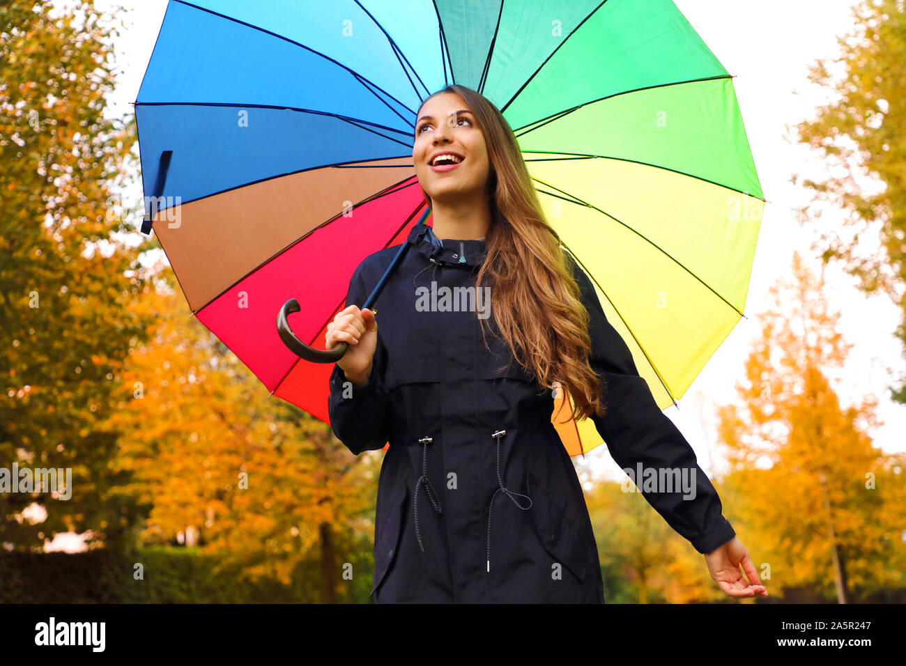 Glückliches Mädchen unter Regenbogen Regenschirm. Herbst Frau wandern in Forest Park im Freien mit Regenbogen Regenschirm. Stockfoto