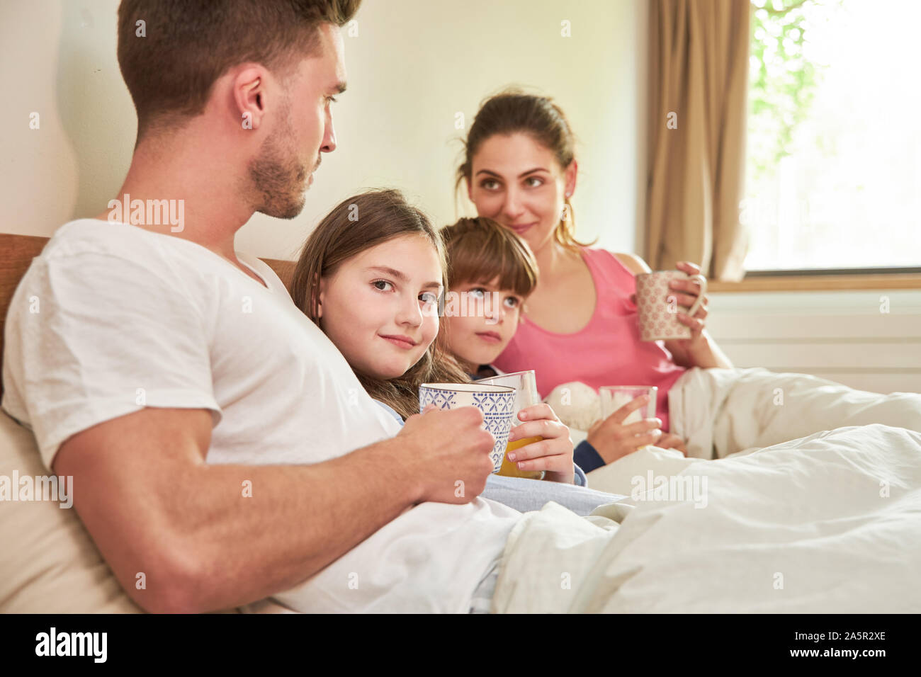 Eltern und zwei Kinder, Frühstück am Morgen im Bett im Schlafzimmer Stockfoto