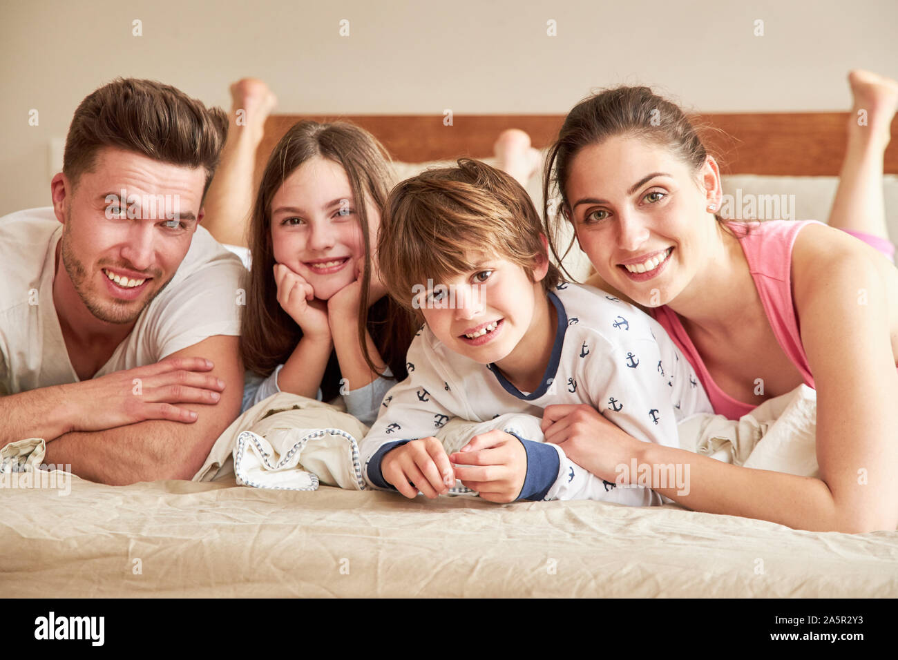 Glückliche Eltern mit zwei Kindern im Schlafanzug morgens im Bett Stockfoto