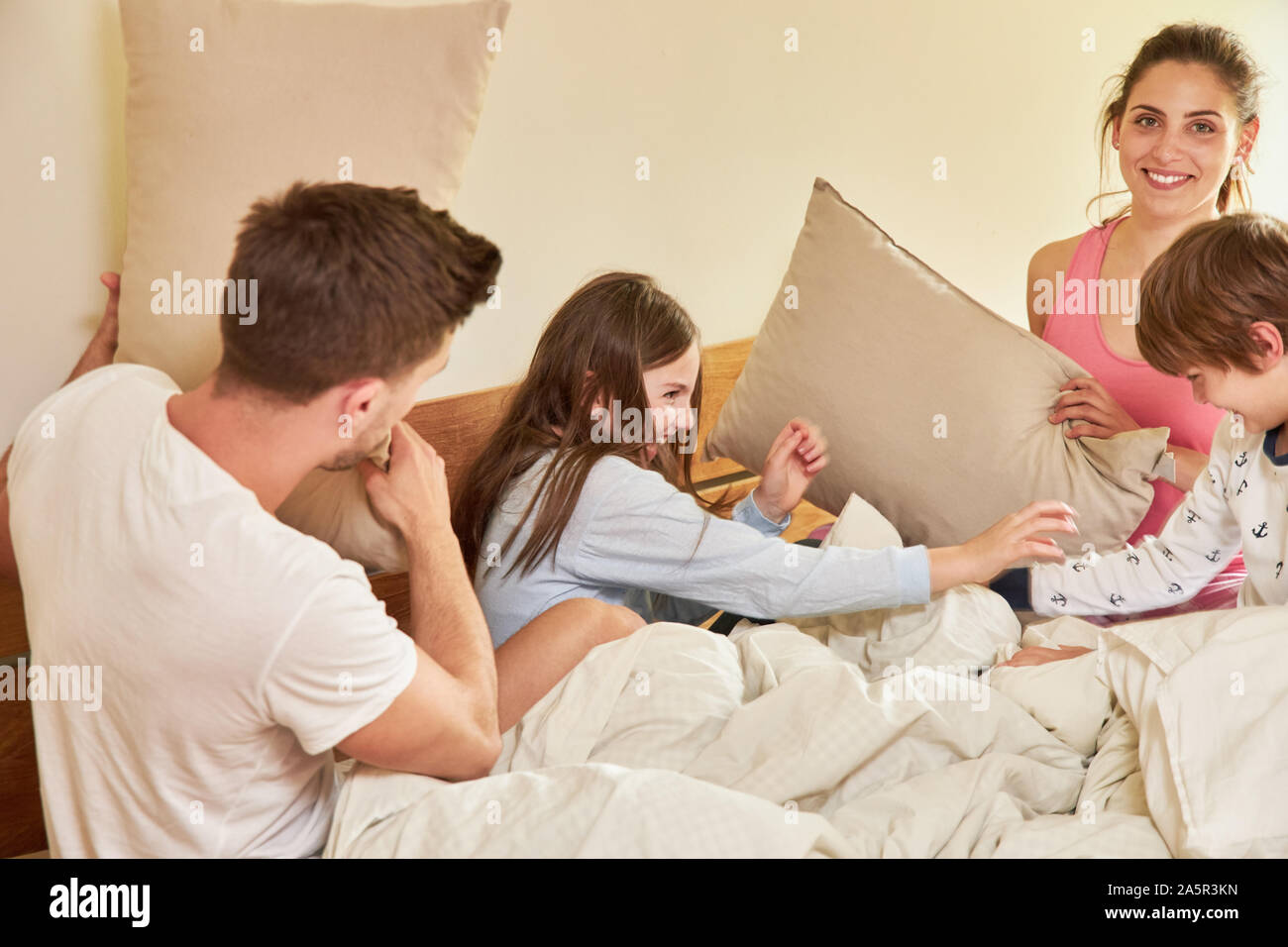 Glückliche Eltern und zwei Kindern viel Spaß beim Kampf gegen die Kissen im Bett Stockfoto