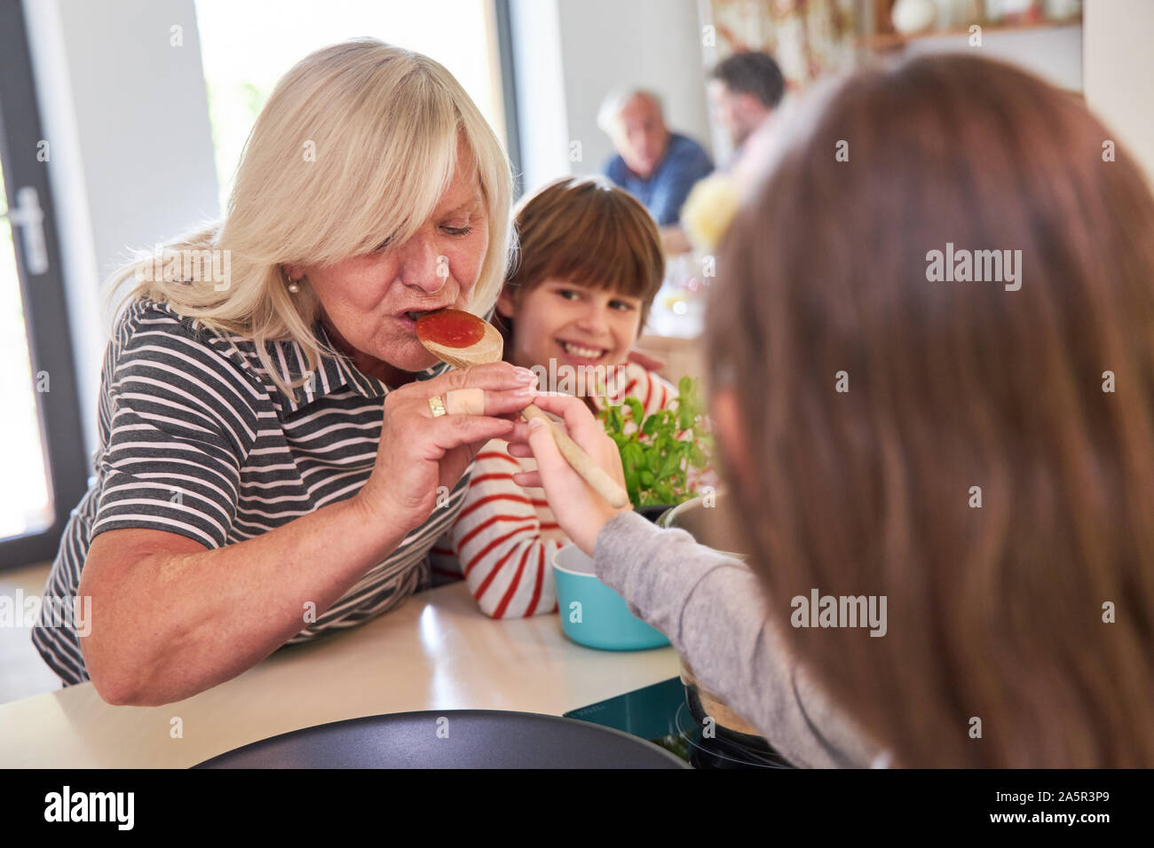 Oma und Kinder Kochen und Würzen die Tomatensauce in der Küche Stockfoto