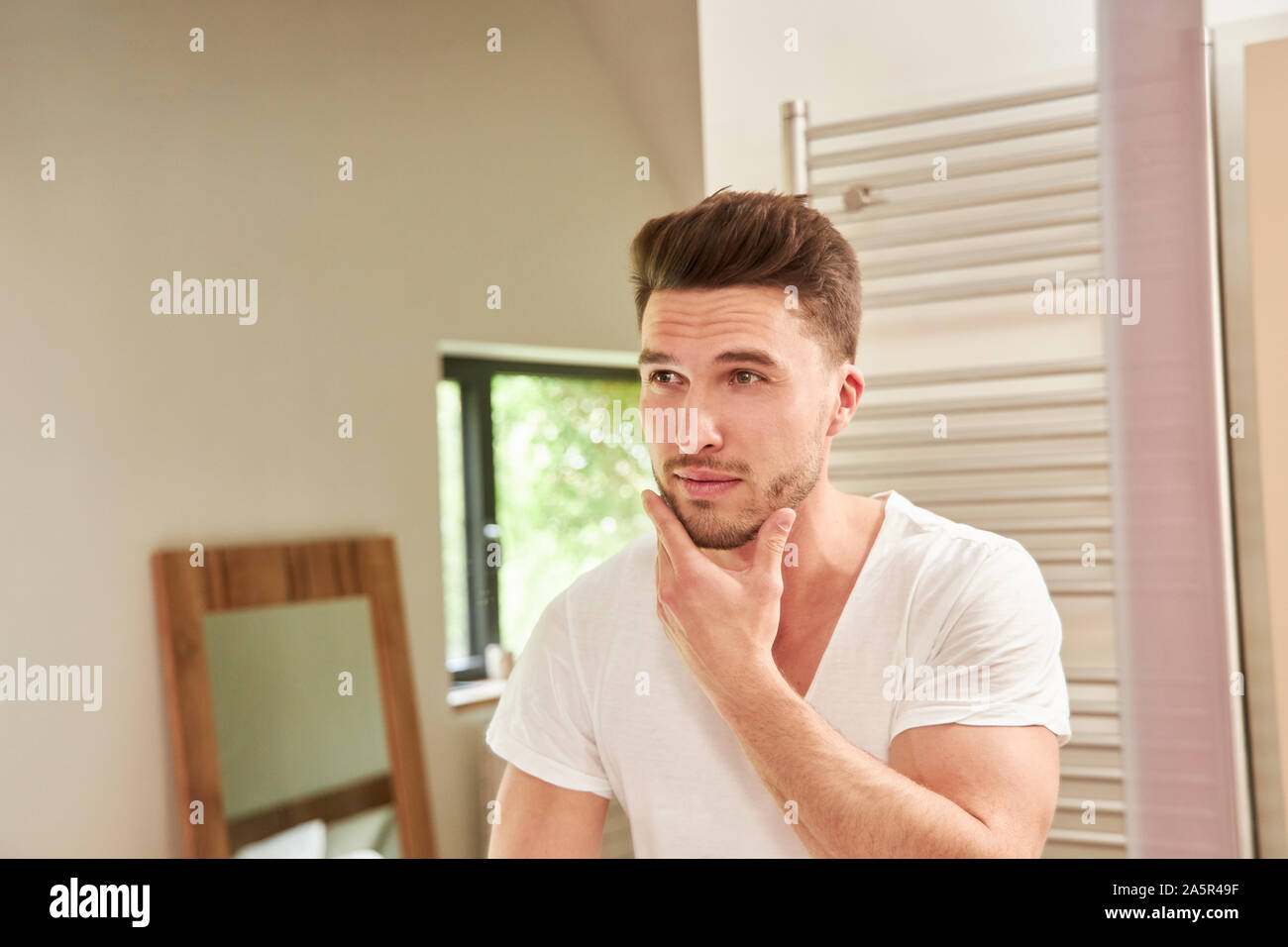 Junger Mann mit drei-Tage-Bart im Badezimmer vor dem Spiegel Stockfoto