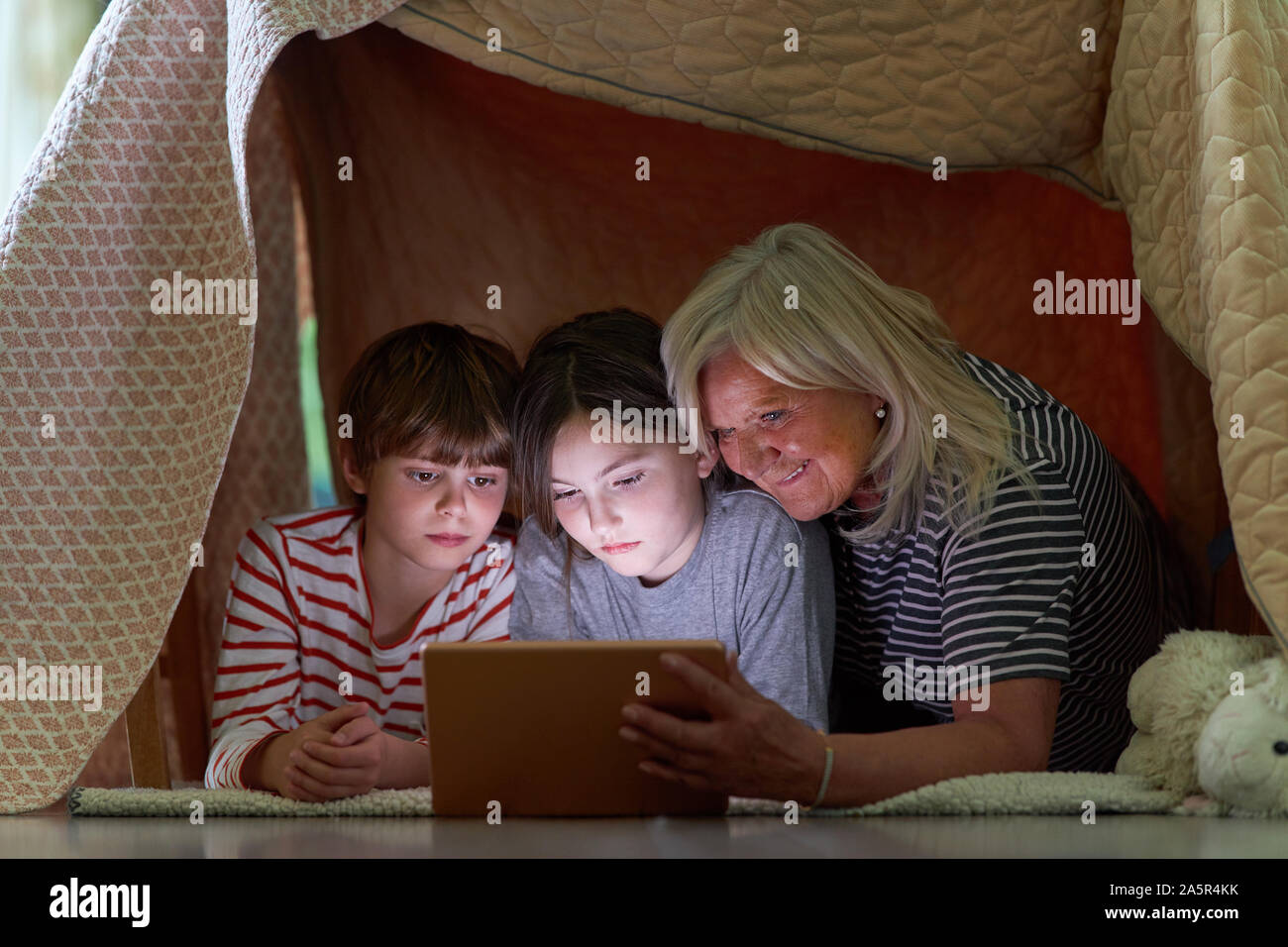 Kinder und Oma mit Tablet Computer beim Surfen im Internet unter Decke wie ein Zelt Stockfoto