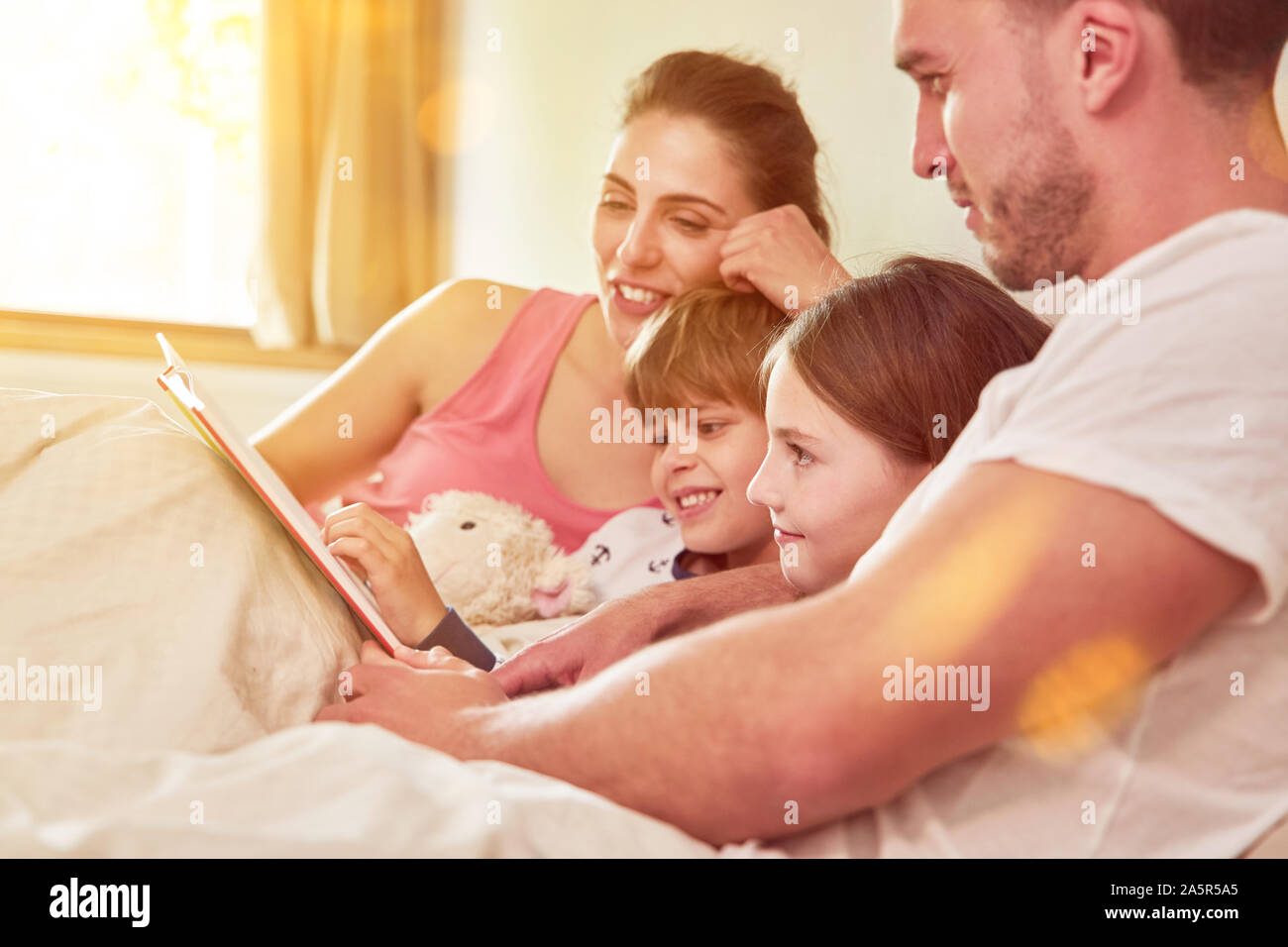Zwei Kinder in der Familie erhalten Buch lesen im Bett der Eltern Stockfoto