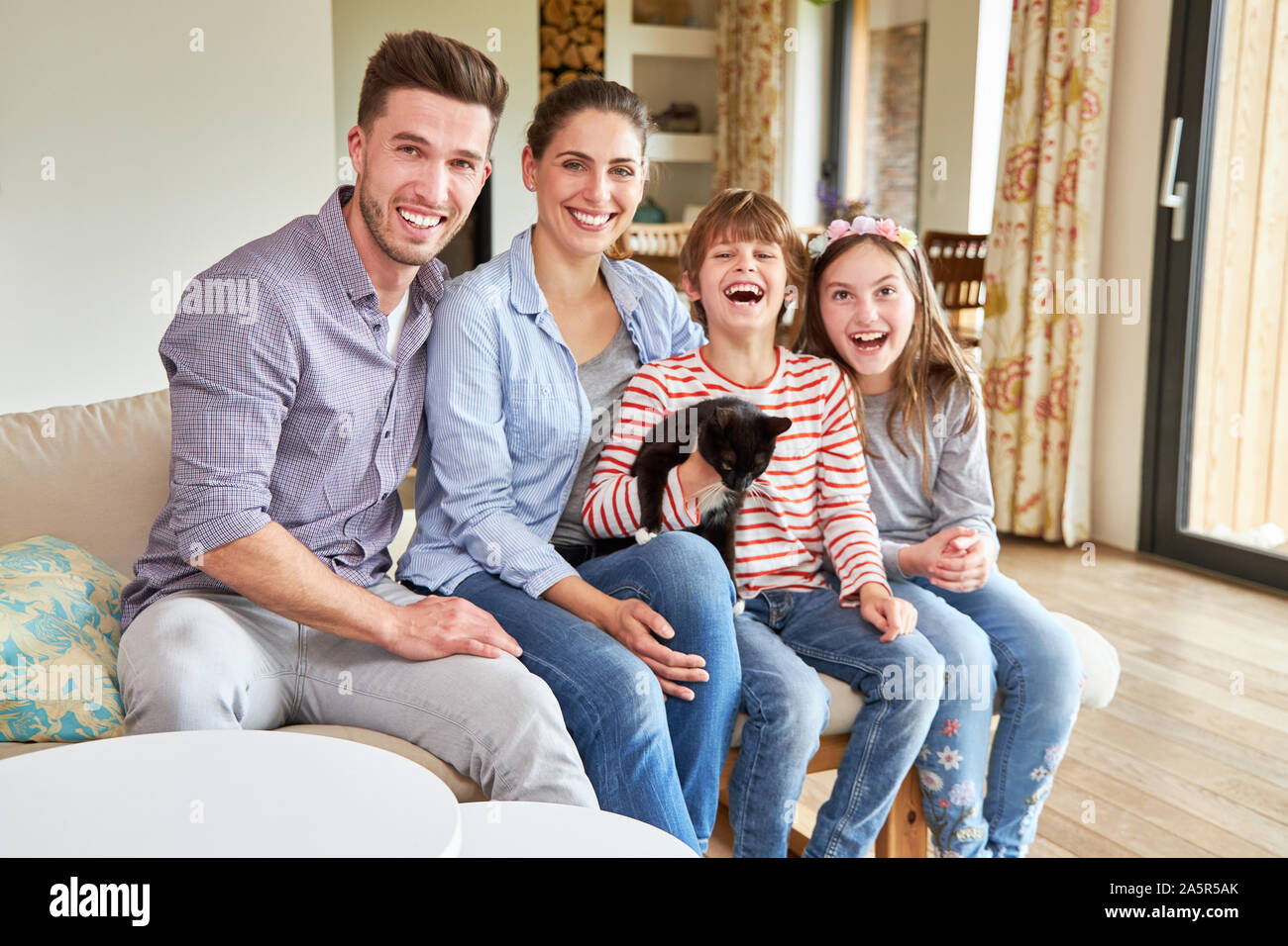 Eltern und zwei Kinder mit einer kleinen Katze sind glücklich lachend sitzen im Wohnzimmer Stockfoto