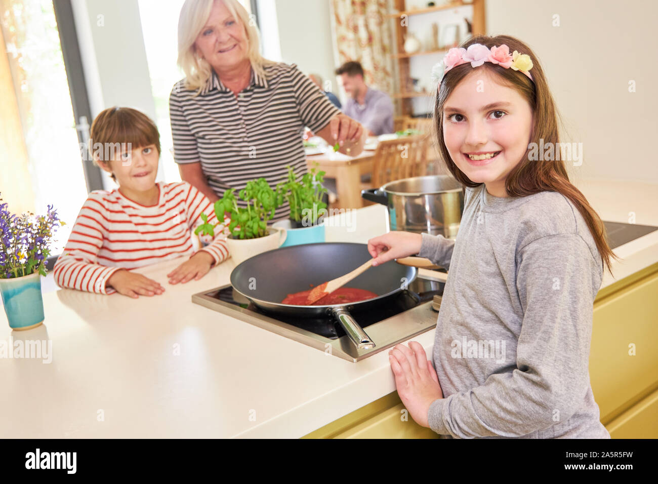 Mädchen Köche Tomatensauce zusammen mit ihrem Bruder und die Hilfe der Oma Stockfoto