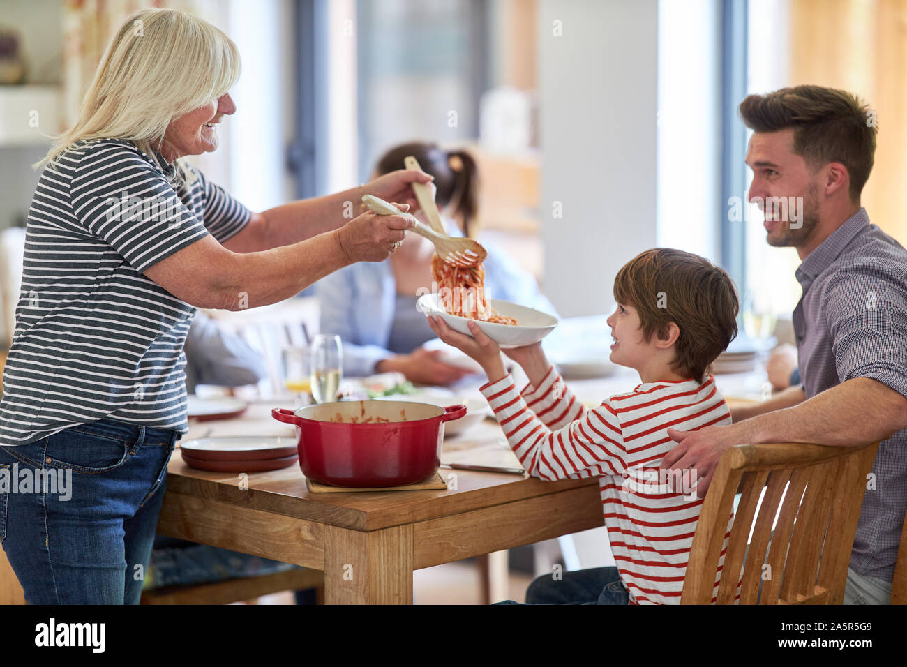Kind als Enkel bekommt eine Portion Spaghetti von der Großmutter am Esstisch Stockfoto