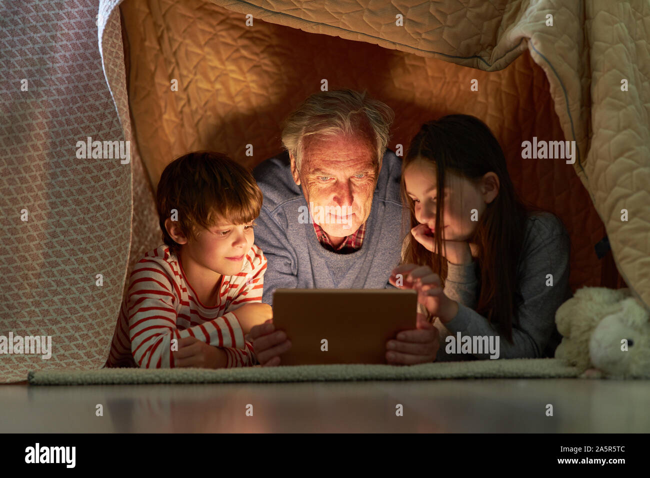 Kinder und Großvater mit Tablet-PC oder e-book unter eine Decke wie ein Zelt Stockfoto