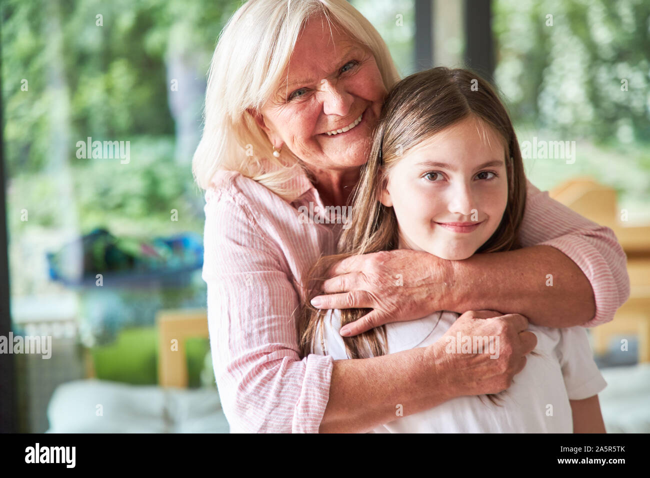 Oma liebevoll umarmt ihre Enkelin im Wohnzimmer zu Hause. Stockfoto