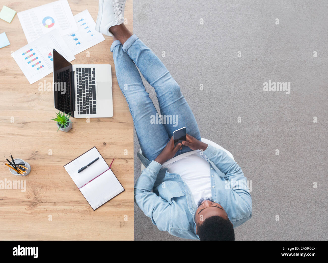 Unvorsichtige Mitarbeiter mit Smartphone und seine Beine auf dem Tisch halten. Stockfoto