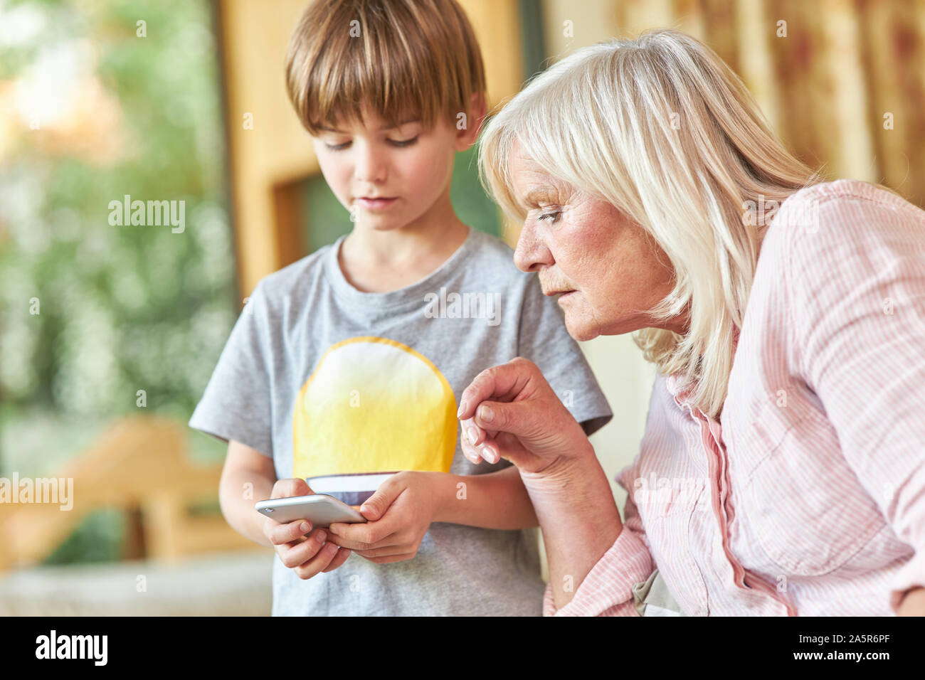 Ältere Frau schaut neugierig an die Enkel Smartphone und liest eine SMS Stockfoto