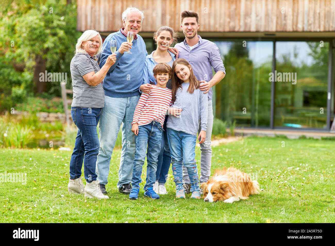 Erweiterte Familie mit Großeltern und Kinder feiern mit Sekt im Garten Stockfoto