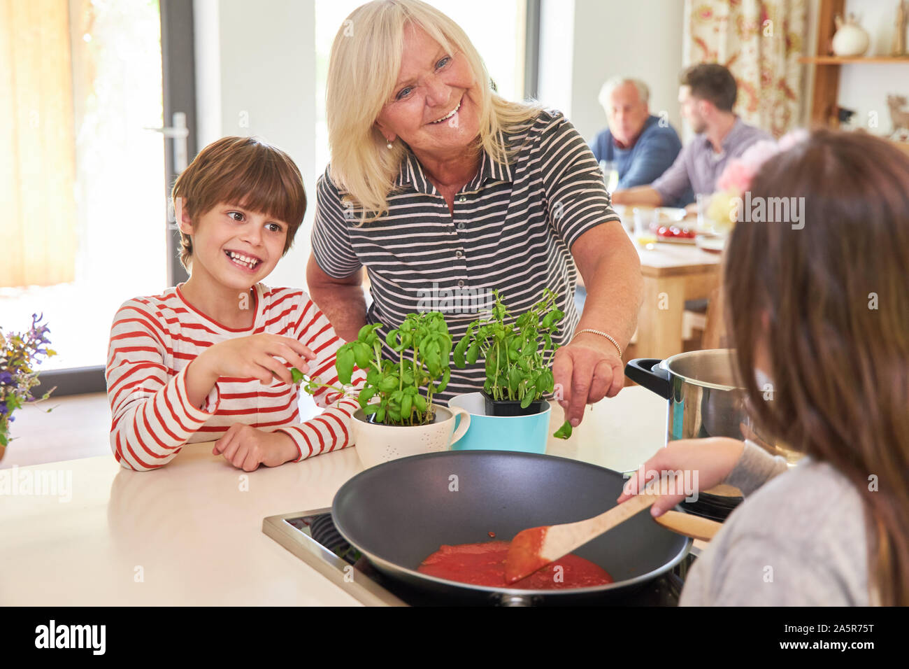 Großmutter kocht Spaghetti mit Tomatensauce und Kräuter mit Enkel Kinder Stockfoto