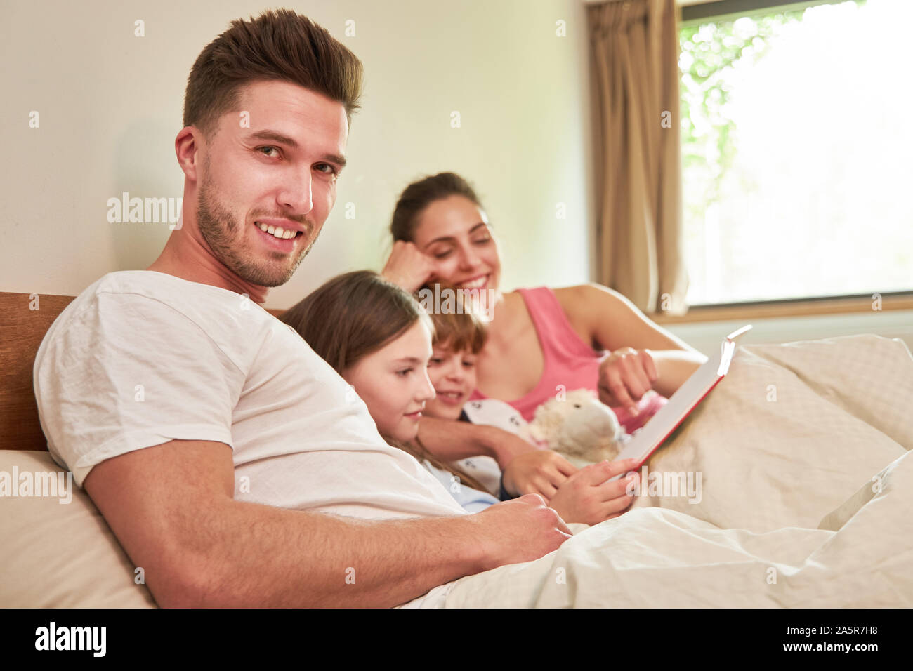 Glückliche Familie mit zwei Kindern mit Buch beim Lesen im Bett zusammen Stockfoto