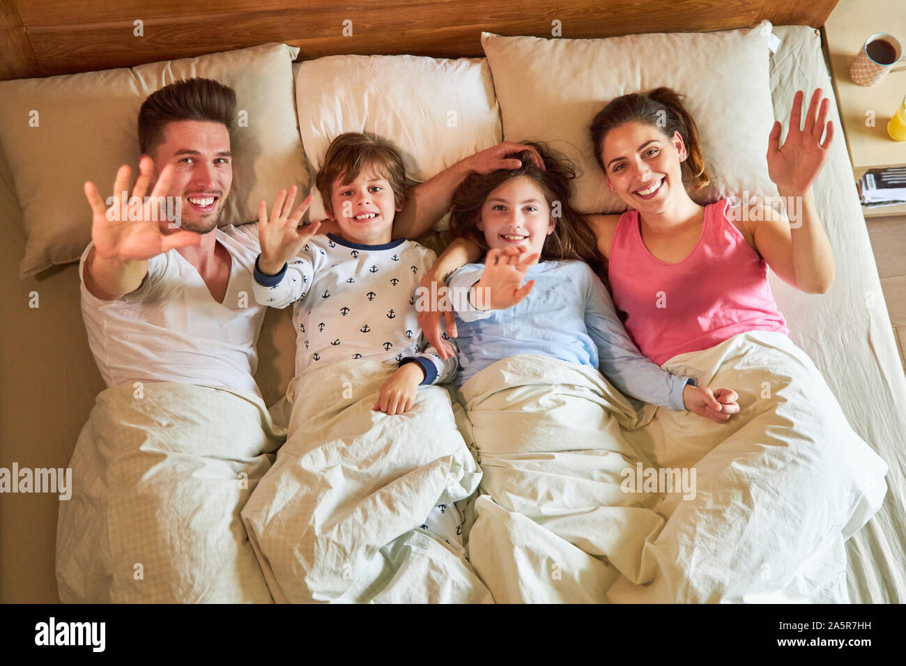 Eltern und zwei Kinder im Bett glücklich Winken in die Kamera Stockfoto
