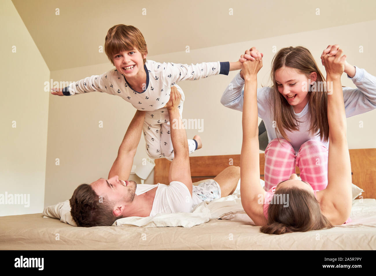 Eltern spielen mit ihren zwei Kindern im Bett am Morgen als Familie zusammen Stockfoto