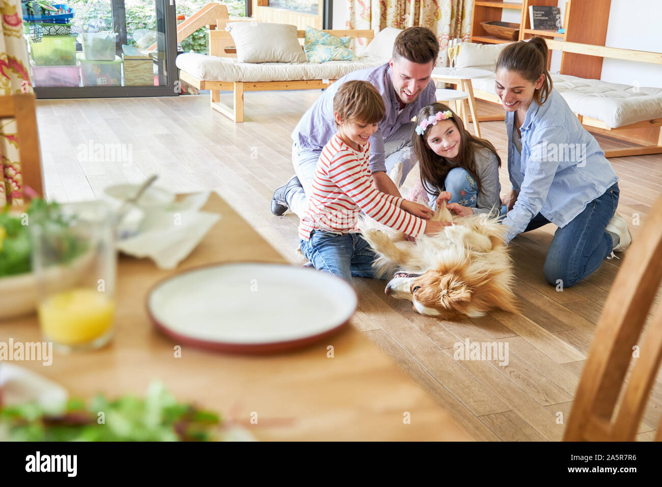 Glückliche Familie und zwei Kinder spielen mit dem Hund im Wohnzimmer Stockfoto