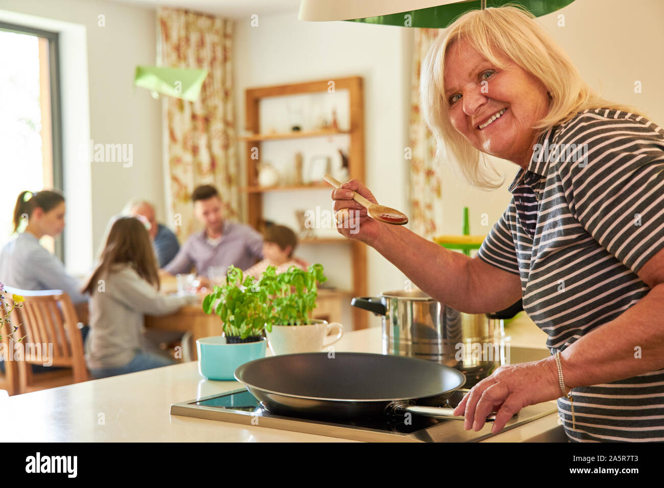 Lächelnde Großmutter beim Kochen und Würzen am Herd in der Küche Stockfoto