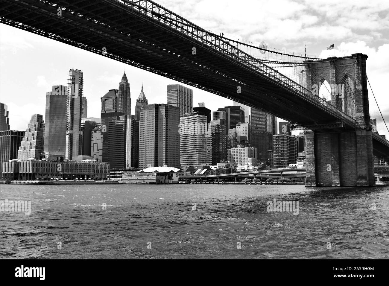 Blick vom East River in New York, der berühmten Brooklyn Bridge, die links von Manhattan nach Brooklyn, vor der Skyline von Downtown Manhattan. Stockfoto