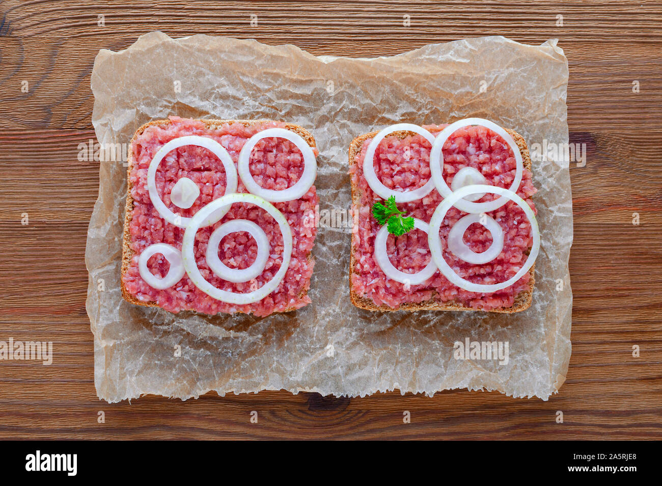Deutsche essen mett Boden Schweinefleisch, Bun- und rohes Fleisch mit Zwiebeln und Petersilie auf Holz- Hintergrund Stockfoto