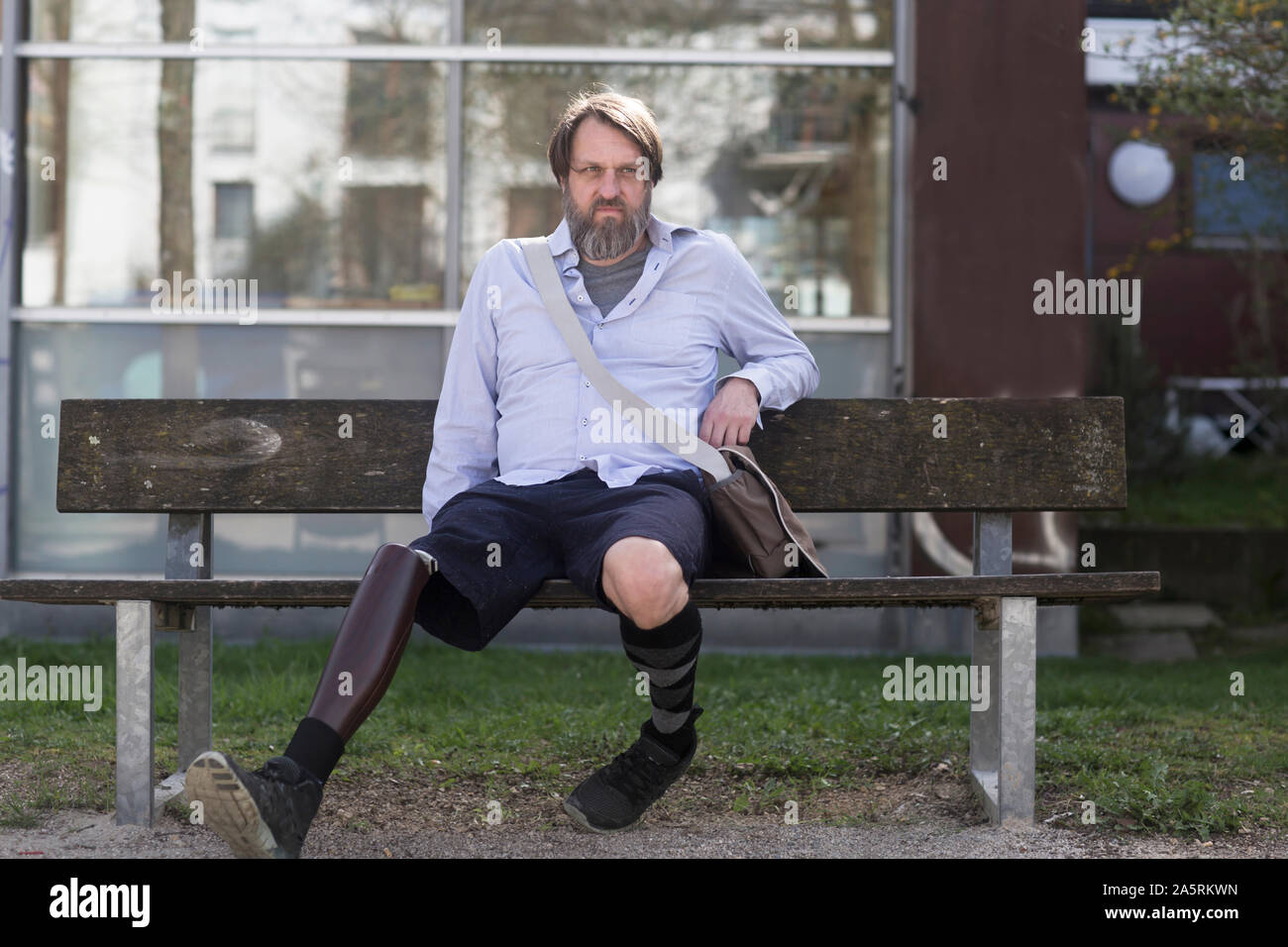 Älterer Mann mit beinprothese, die auf einer Bank sitzen Stockfoto