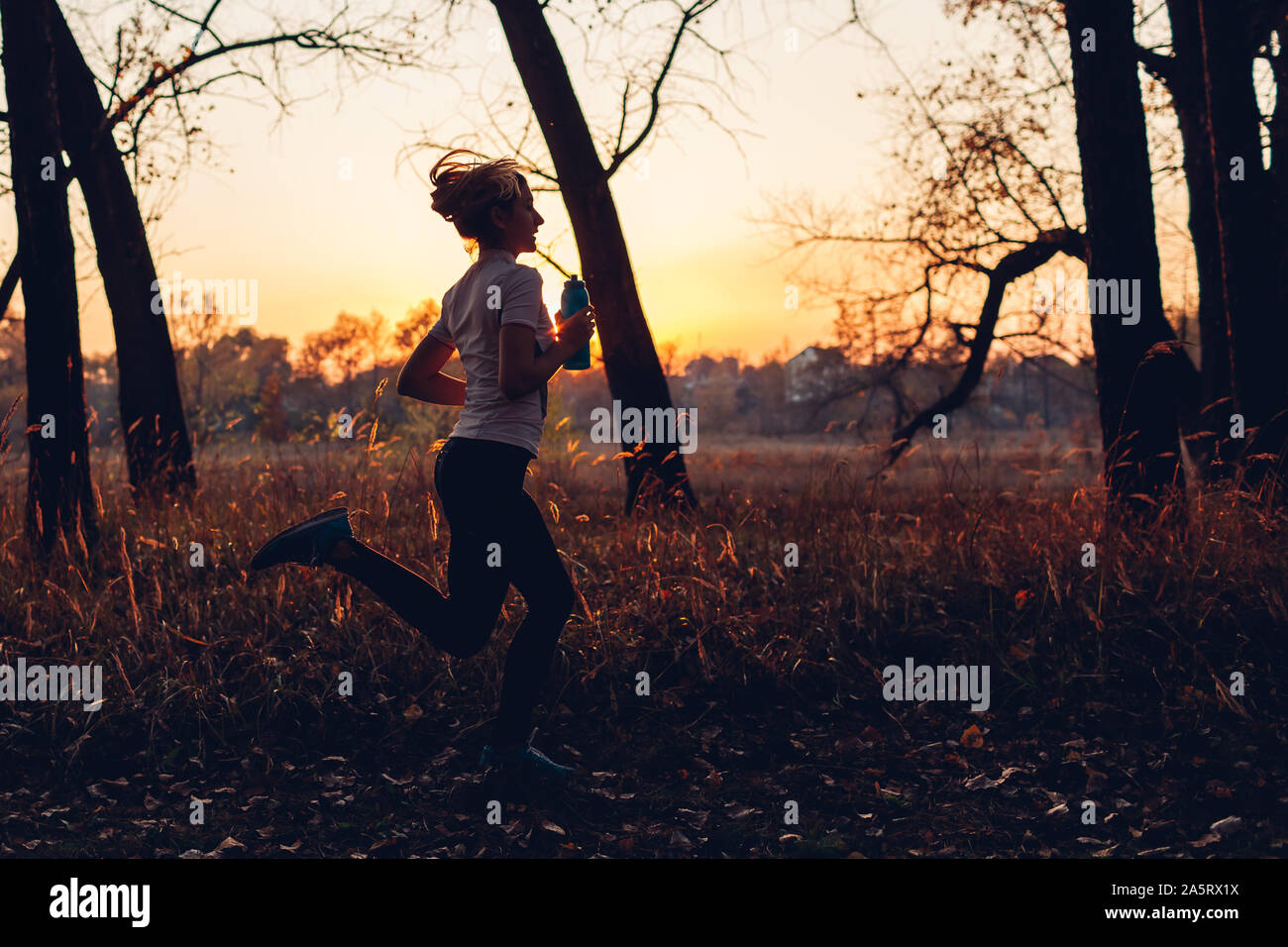 Runner Training im Herbst Park. Frau mit Wasserflasche bei Sonnenuntergang. Aktiver Lebensstil. Silhouette der slim-junges Mädchen Stockfoto