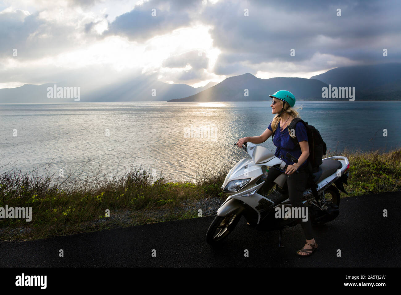 Eine Frau sitzt auf einem Motorrad mit wunderschönen Ozean Szene im Hintergrund. Stockfoto