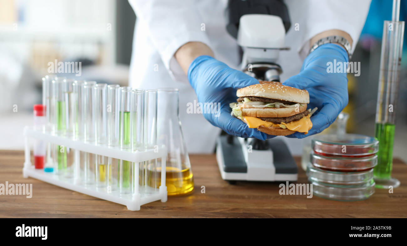 Männliche Hand halten Burger in der Hand mit blau Schutzhandschuhe Stockfoto