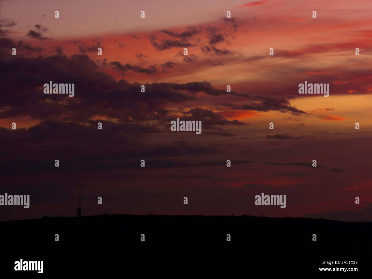 Sonnenuntergang über einem Hügel. Riesige dunkle mystische Wolken. Orange, Pink und Pfirsichfarben wechseln sich ab. Schwarze Silhouette des Hügels am unteren Bildrand. Stockfoto