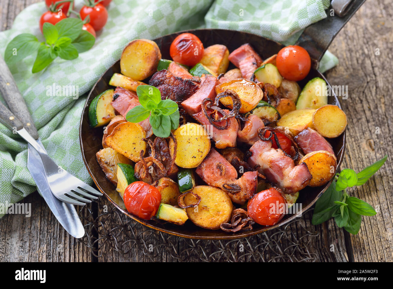 Eine Füllung Essen: Gebratene ungeschält baby Kartoffeln mit geräuchertem Schweinefleisch Hals und Gemüse, in eine eiserne Pfanne serviert pan Stockfoto