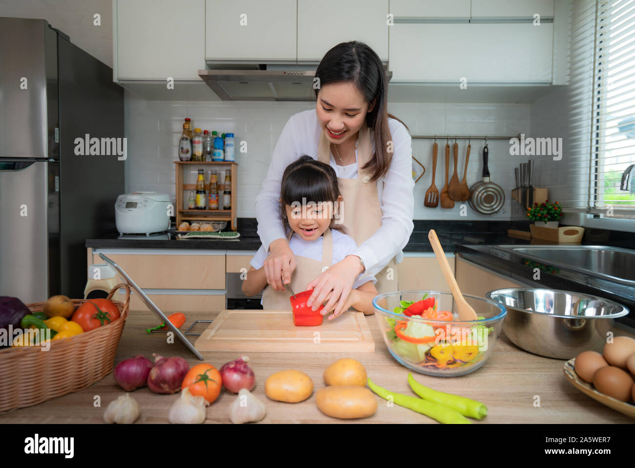 Portrait von schöne asiatische junge Frau und ihre Tochter kochen Salat zum Mittagessen und Schneiden rote Glocke Peper, während sie essen, Familie leben Liebe Relati Stockfoto