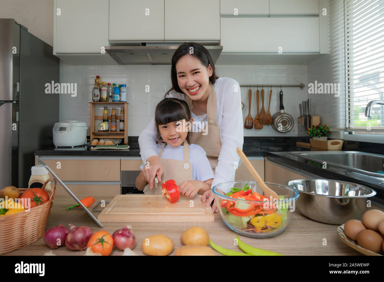 Portrait von schöne asiatische junge Frau und ihre Tochter kochen Salat zum Mittagessen mit online-Internet in einer digitalen Tablet suche Rezept während der f Stockfoto