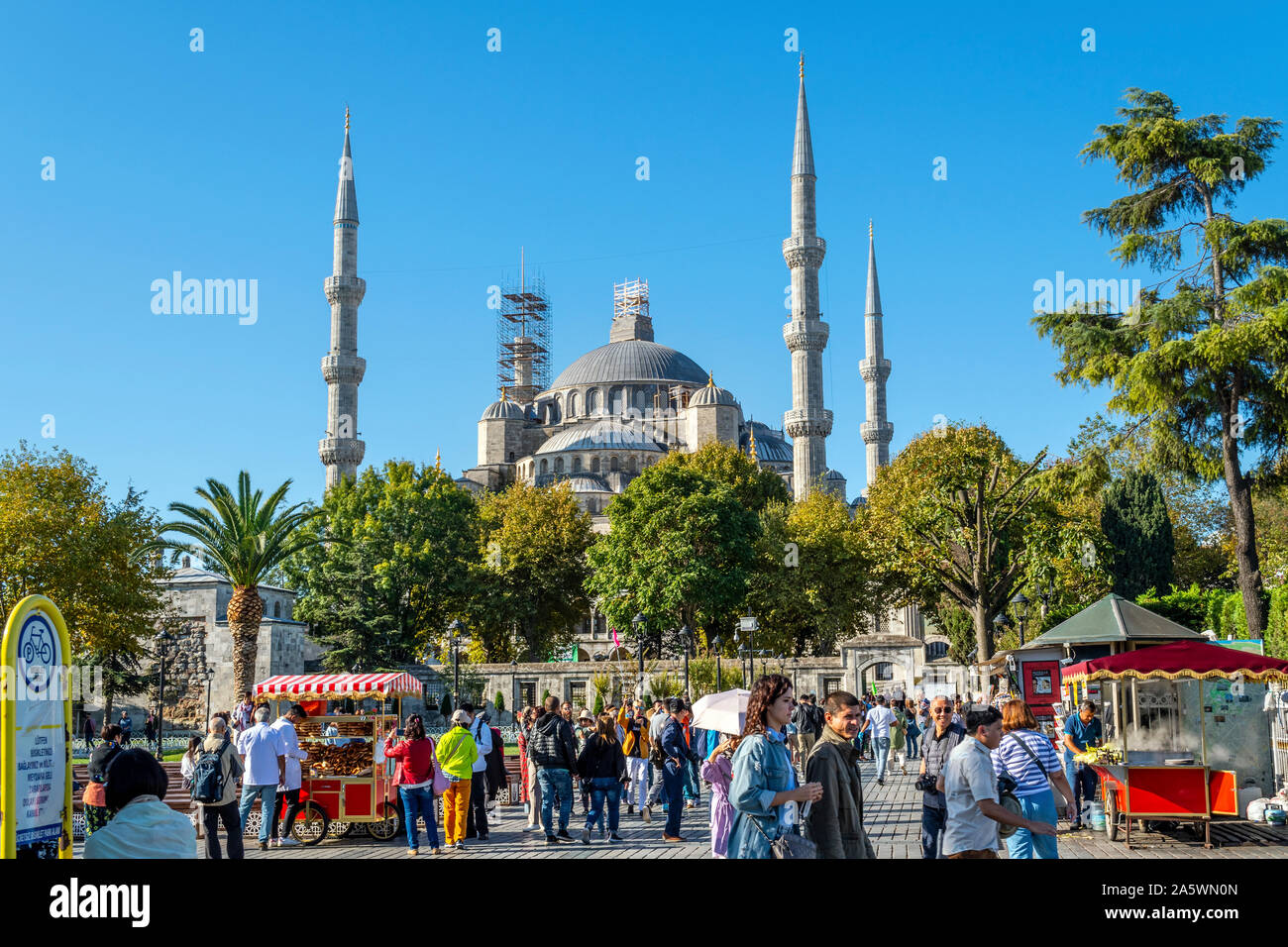 Touristen und Einheimische Türken geniessen Sie einen sonnigen Tag in Sultanahmet Platz unter den gerösteten Maiskolben essen Anbieter steht und der Blauen Moschee hinter Stockfoto