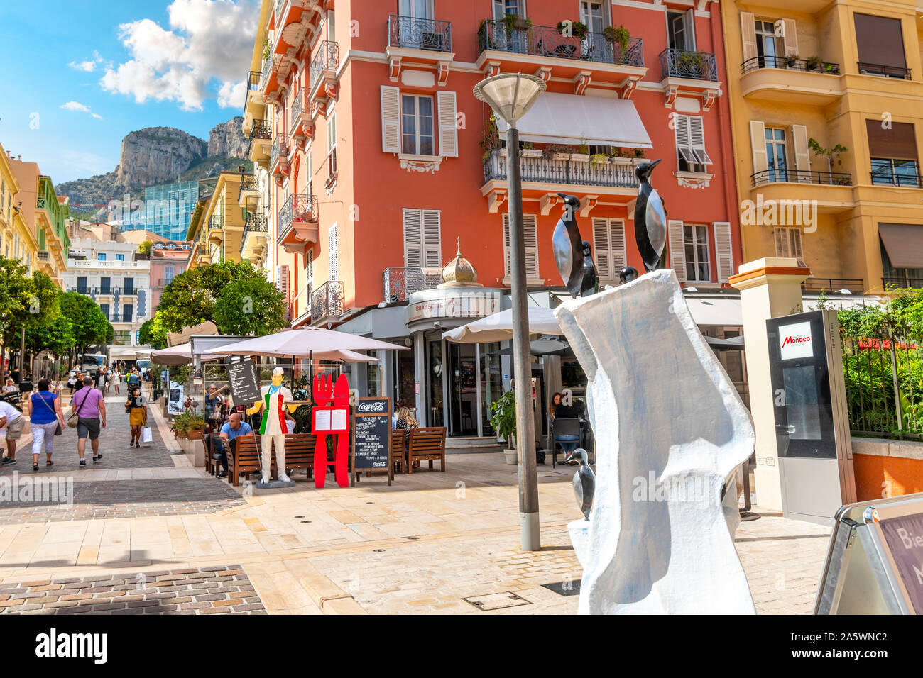 Touristen und Einheimische Monegassischen einem sonnigen Sommertag genießen Sie Shopping und Dining in Monte Carlo, Monaco, mit der steilen Berge in der Ferne. Stockfoto