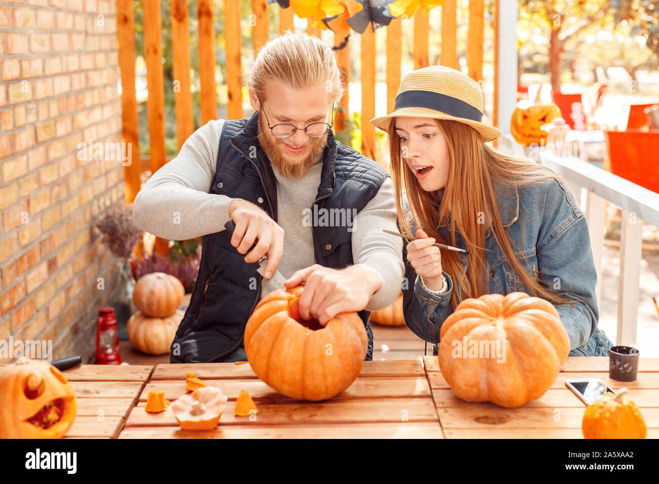 Halloween Einlieferung am Konzept. Junges Paar sitzen am Tisch im Freien, die Jack-o'-Lantern Kerl Carving pumpking, während Mädchen beobachten beeindruckt Stockfoto