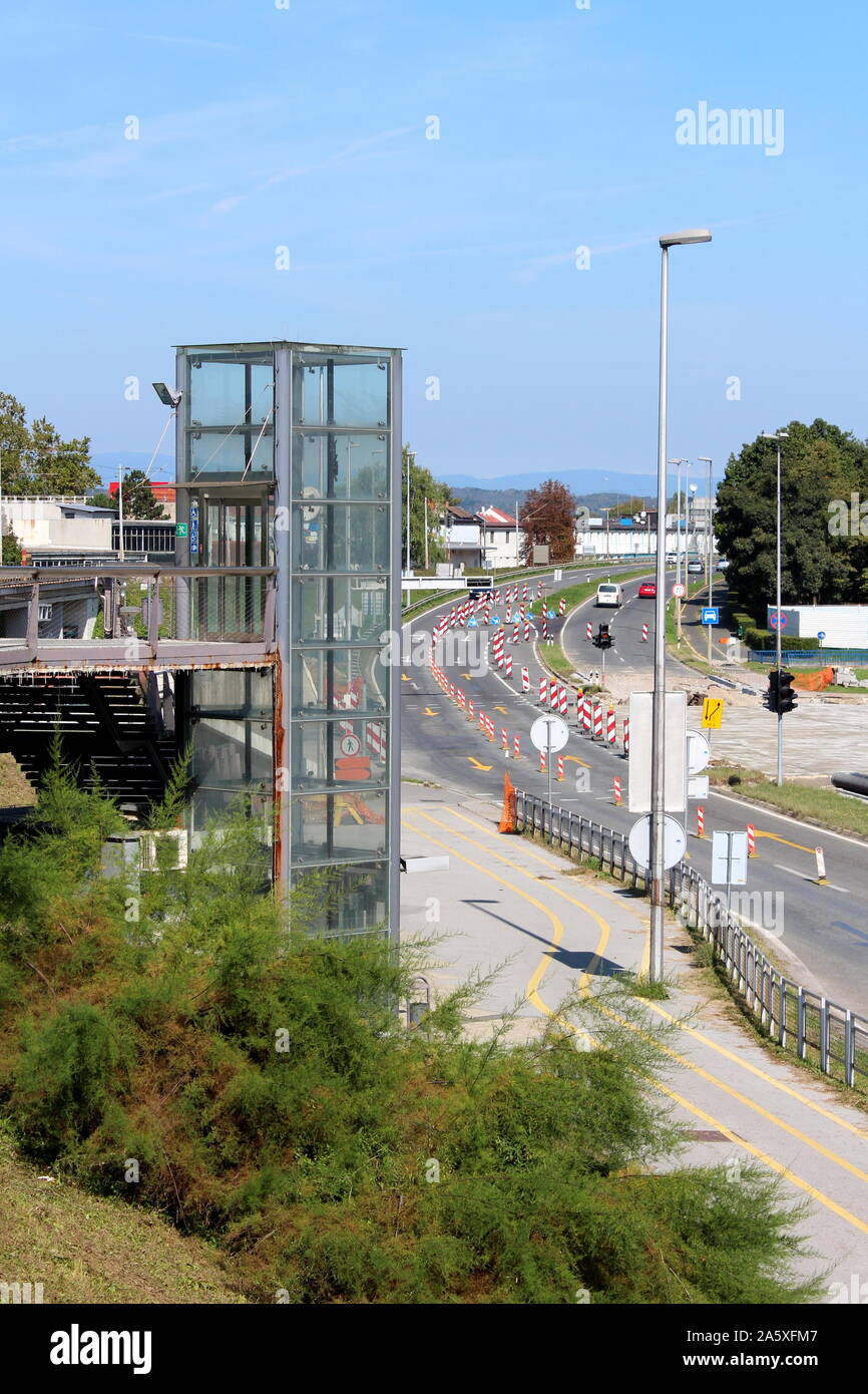 Aufzug aus Glas an der Seite der Bahnhof mit dichter Vegetation und Straße unter Rekonstruktion mit mehreren Warnung Verkehrszeichen umgeben Stockfoto