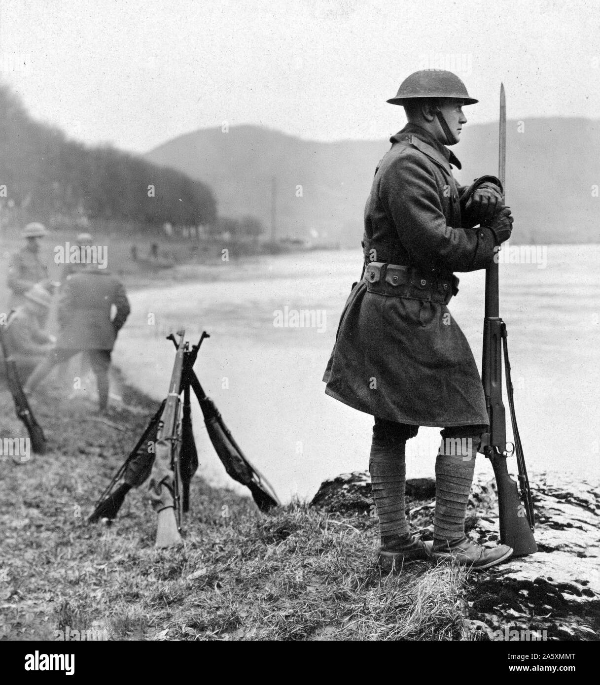 "Die UHR AUF DEM RHEIN" SENTRY auf einem Felsen am Ufer des Flusses ruht auf sein Gewehr gestellt und aus der Suche über Wasser ca. 1/18/1919 Stockfoto