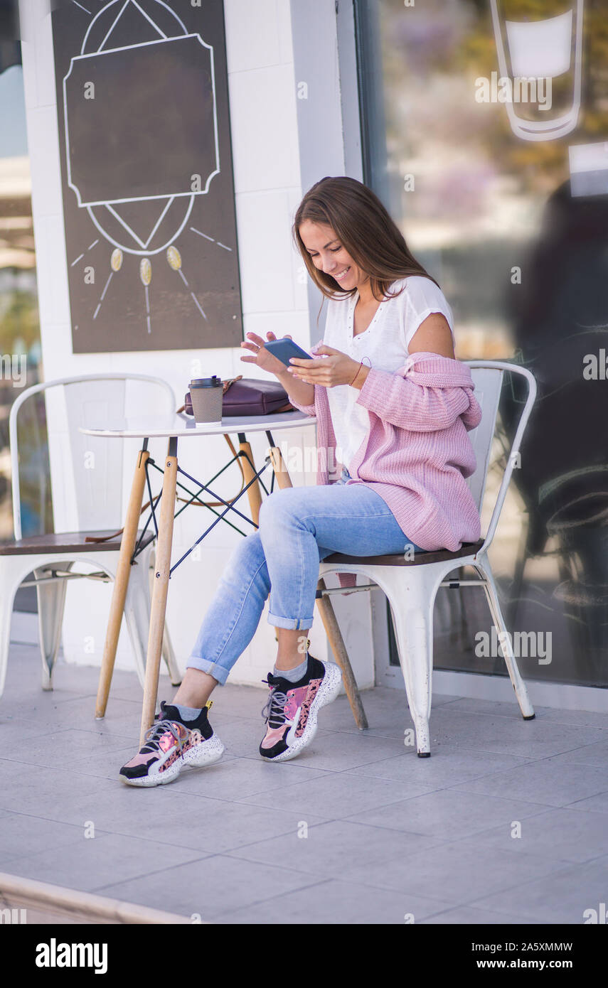 Frau mit Smartphone und Tasse Kaffee draußen auf der Straße Cafe zu gehen. Glücklich lächelnde Mädchen. Stockfoto