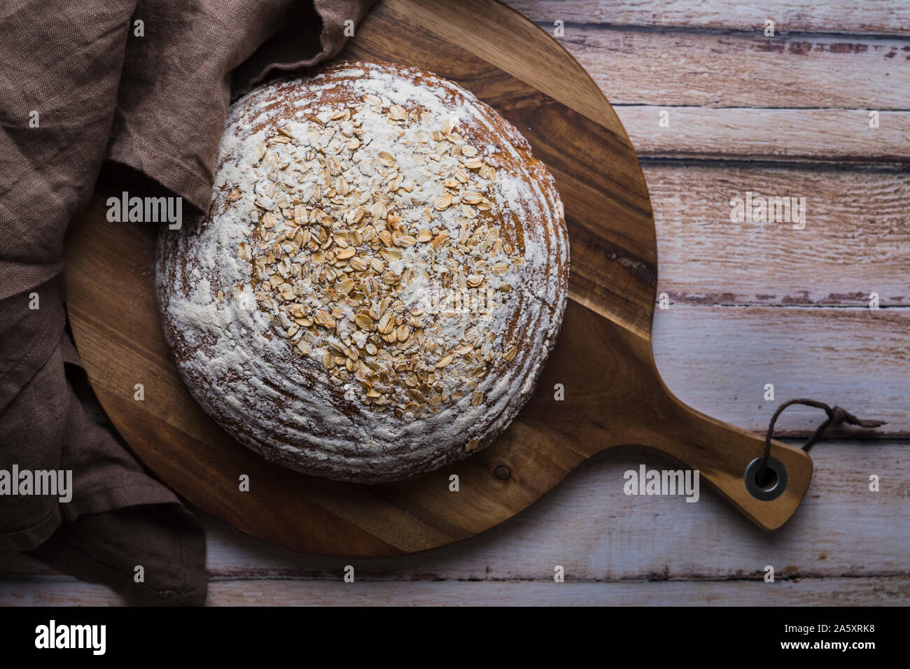 Hausgemachte organische Sauerteigbrot von oben, flach gesehen legen Perspektive. Die rustikale Brot hat Haferflocken auf der Oberseite, und ist auf einem hölzernen Schneidebrett festgelegt Stockfoto