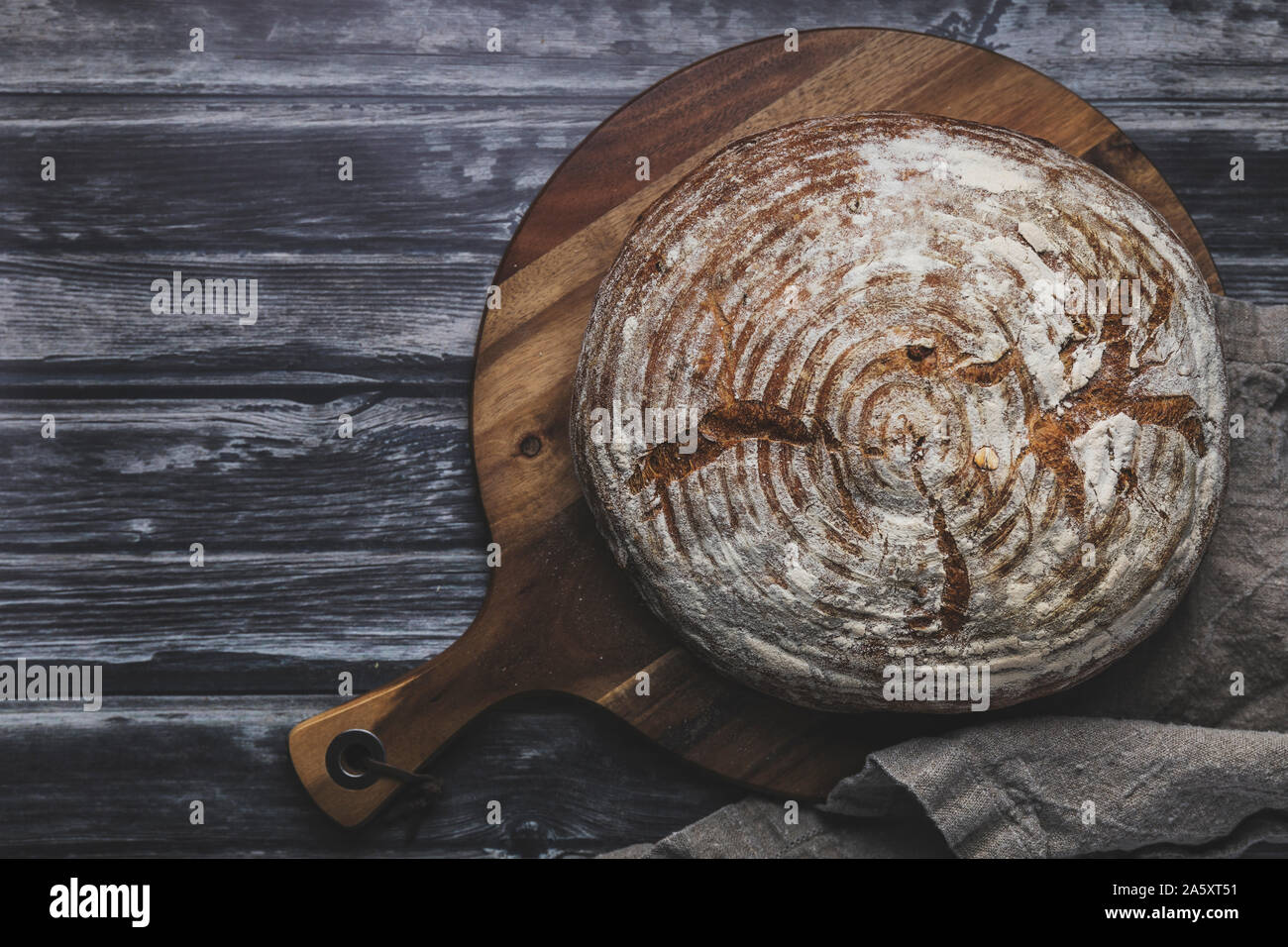 Hausgemachte organische Sauerteigbrot von oben, flach gesehen legen Perspektive. Die gebrochene Rustikales Brot ist auf einem hölzernen Schneidebrett, auf einem rustikalen dunklen Stockfoto
