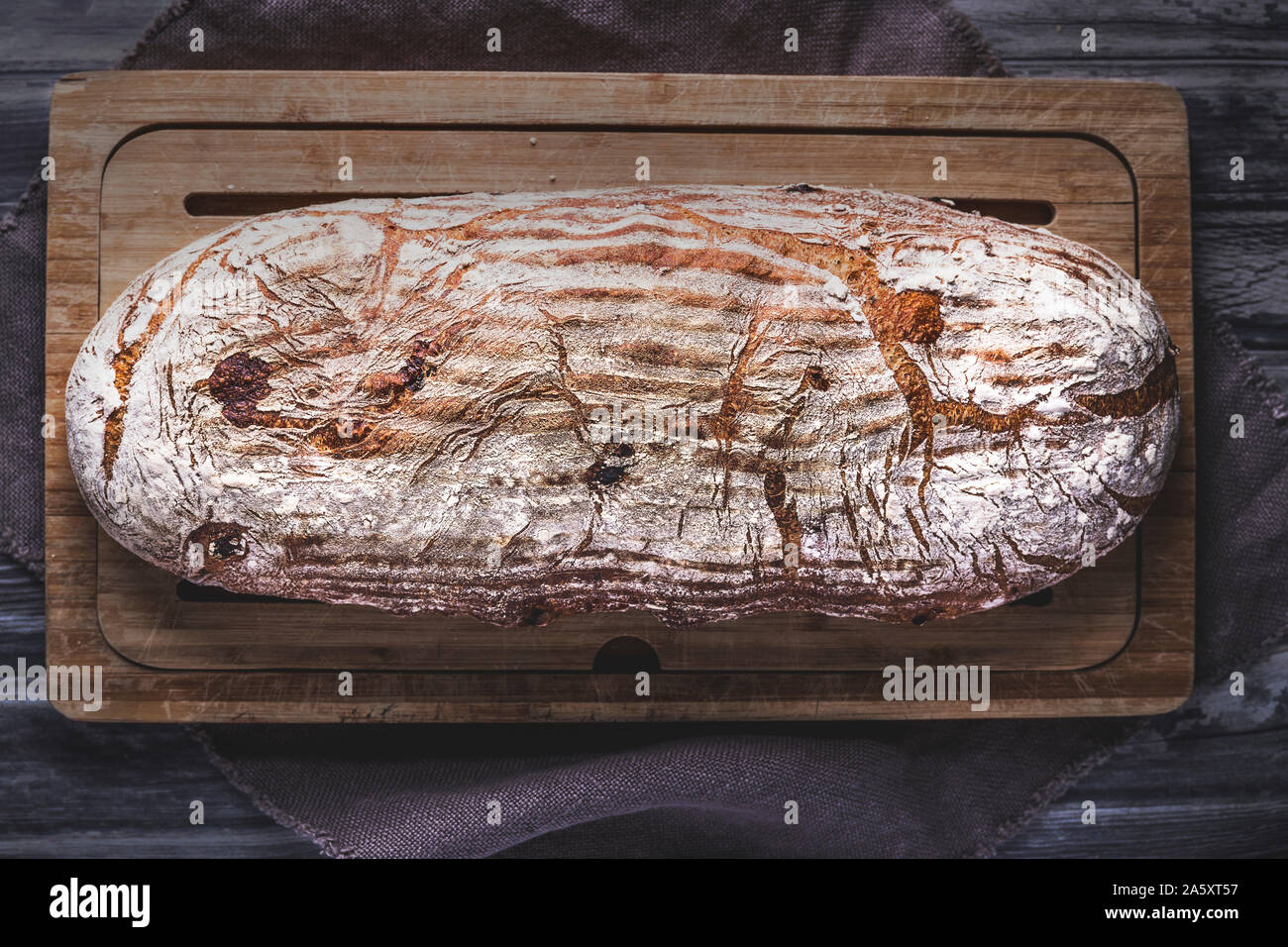 Hausgemachte organische Sauerteigbrot von oben, flach gesehen legen Perspektive. Die gebrochene Rustikales Brot ist auf einem hölzernen Schneidebrett gelegt, neben einem Bettwäsche cl Stockfoto
