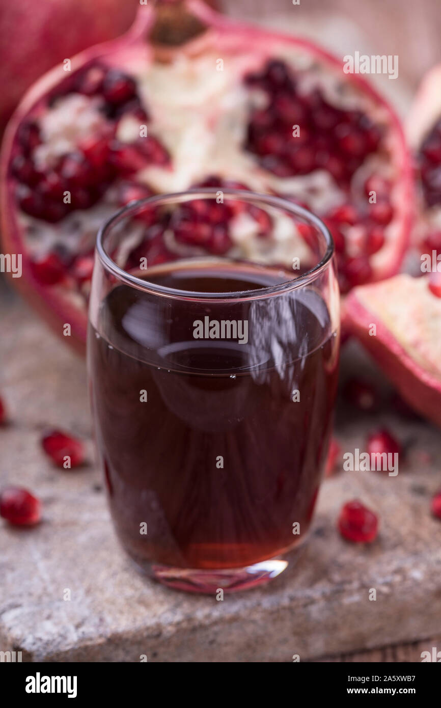 Ein Glas gesunde organische Granatapfelsaft, vor einer halbiert Granatapfel. Obst und Saft werden auf einem rustikalen Stein Oberfläche. Vertikale Ansicht Stockfoto